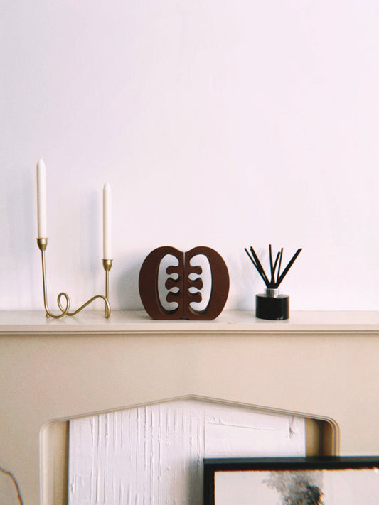 Decorative Ese Ne Tekrema adinkra bookends on a beige fireplace with a gold candlestick and black diffuser.