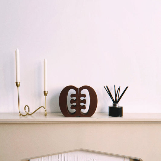 Decorative Ese Ne Tekrema adinkra bookends on a beige fireplace with a gold candlestick and black diffuser.