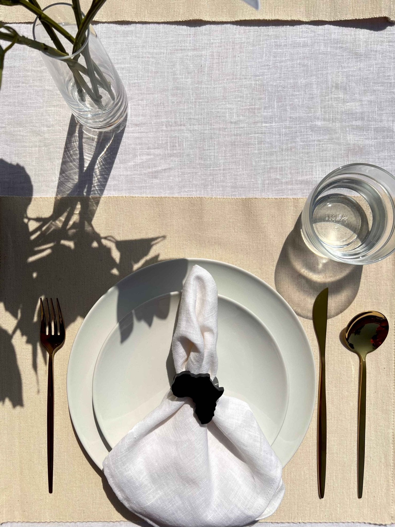 Africa napkin ring in black on an off white plate, glass of water and gold cutlery, on a cream placemat.