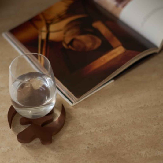 Glass of water on a brown Gye Nyame coaster with an open book in the background