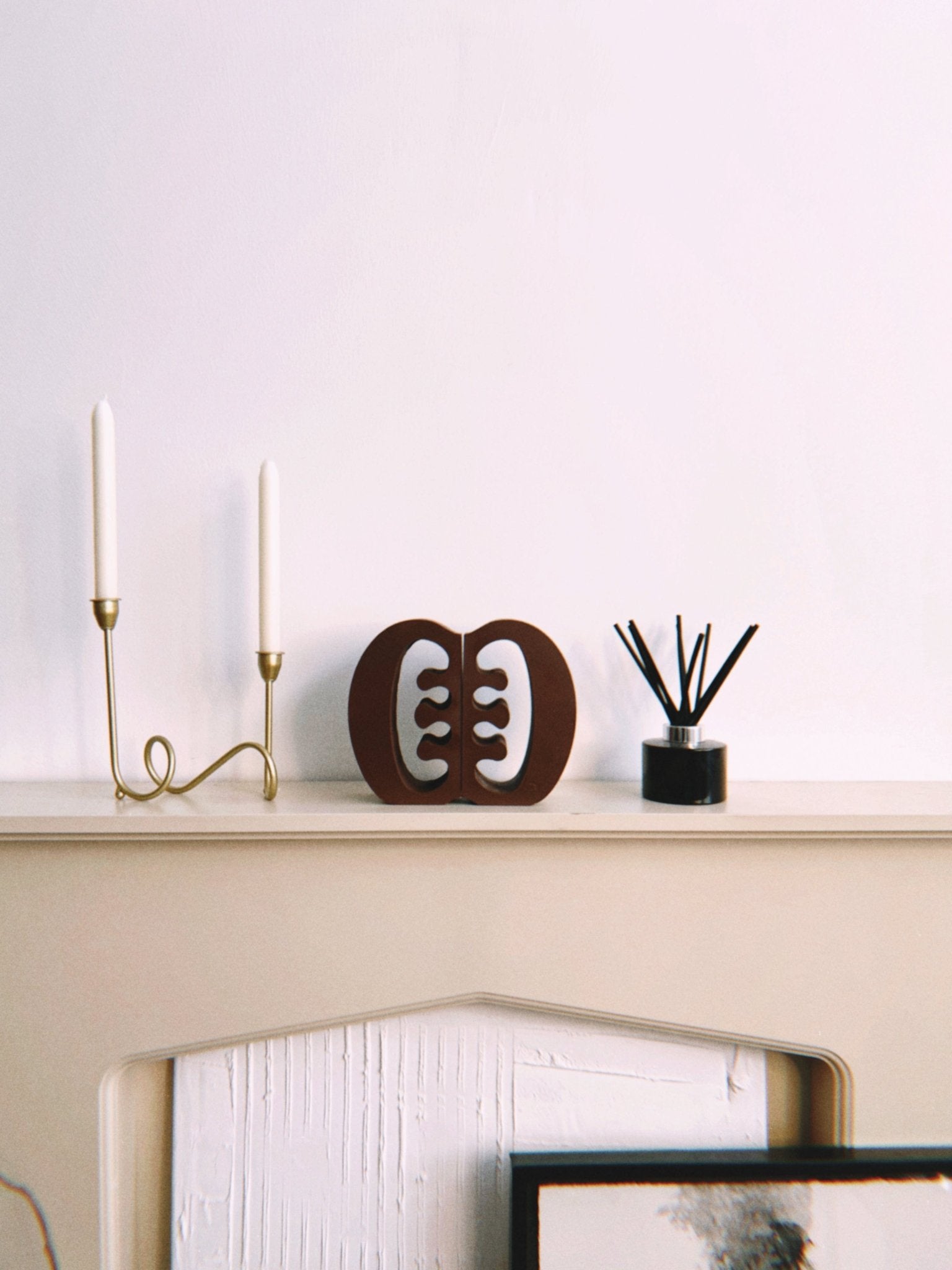 Decorative Ese Ne Tekrema adinkra bookends on a beige fireplace with a gold candlestick and black diffuser.