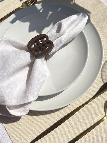  A coffee coloured Ese Ne Tekrema adinkra napkin ring on an off white plate, with gold cutlery.
