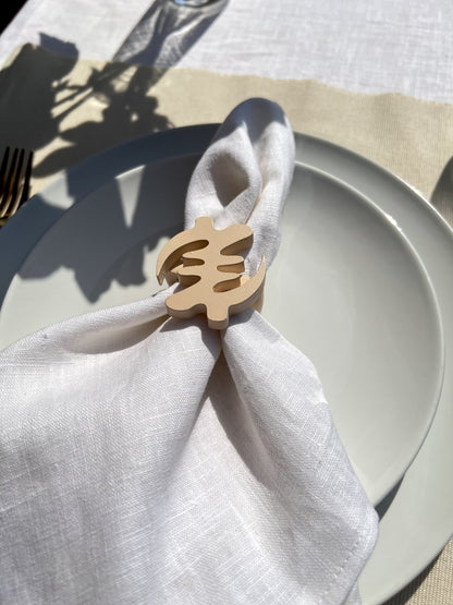 Napkin folded in a cream Gye Nyame adinkra napkin ring on an off white plate with gold cutlery 