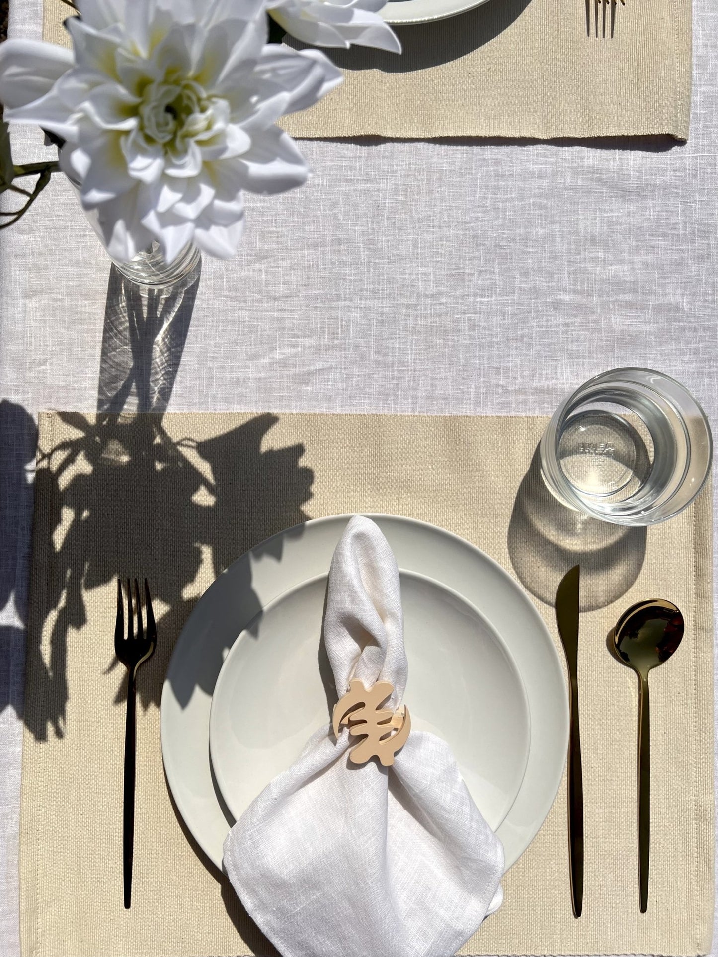 Napkin folded in a cream Gye Nyame adinkra napkin ring on an off white plate with gold cutlery 