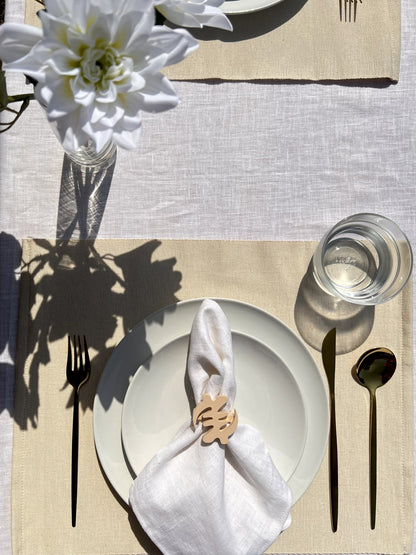 Napkin folded in a cream Gye Nyame adinkra napkin ring on an off white plate with gold cutlery 